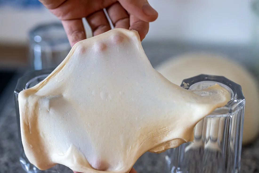 The windowpane test: stretch a piece thin enough to see light through it without tearing. (Photo from The Sourdough Framework.)